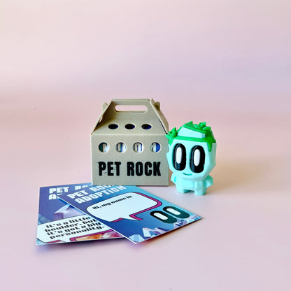 A whimsical green character with large eyes beside a gray carrier and colorful adoption cards on a pink background.