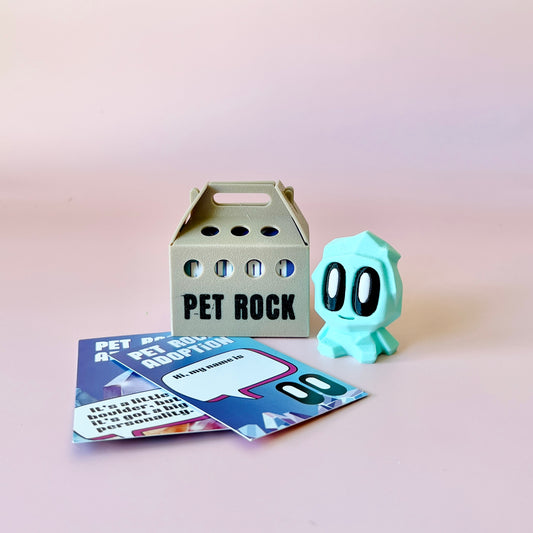 A pastel green blob figure with expressive eyes beside a small carrier and colorful adoption cards on a soft pink background.