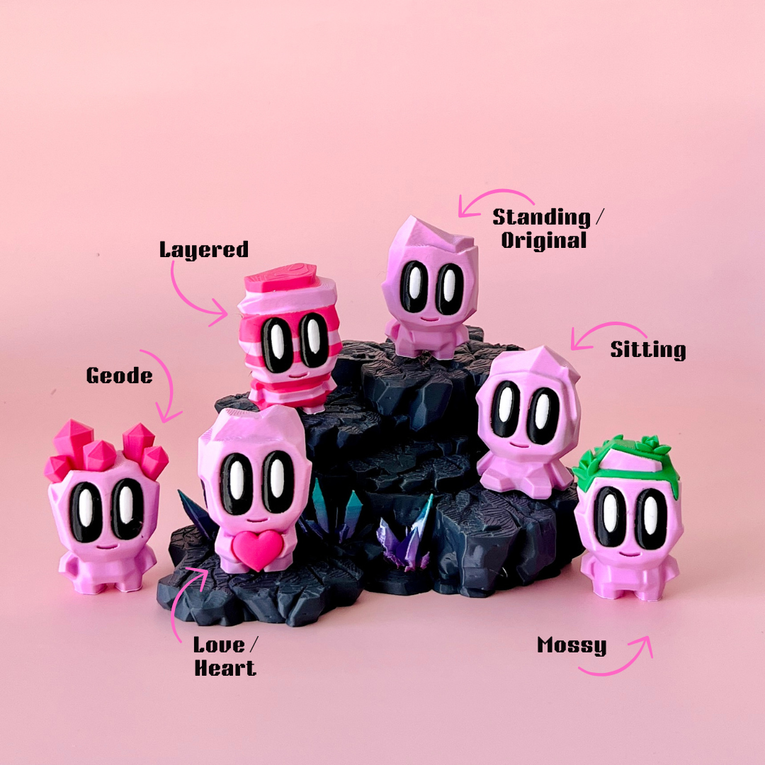 A group of colorful, cartoonish figures on a black rocky base against a soft pink background, showcasing playful designs.