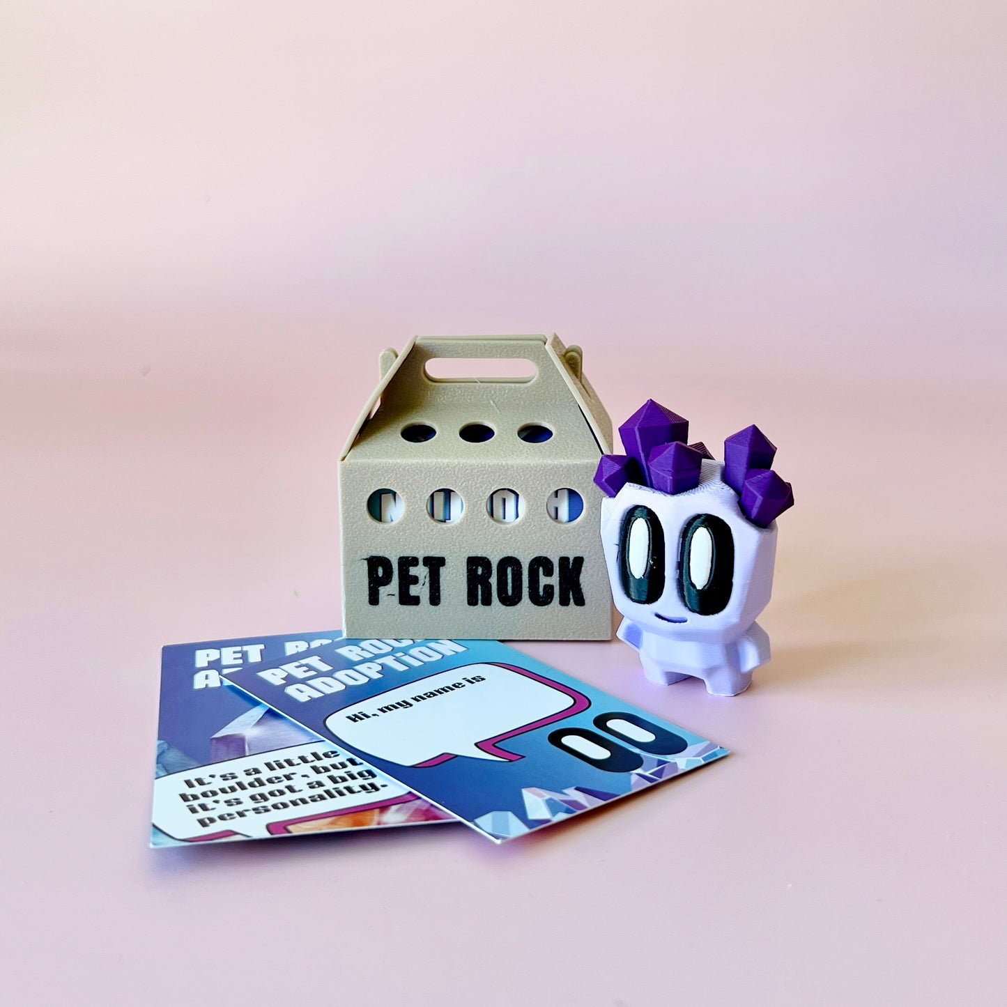A whimsical character with purple crystals on its head beside a cardboard carrier and colorful adoption cards.