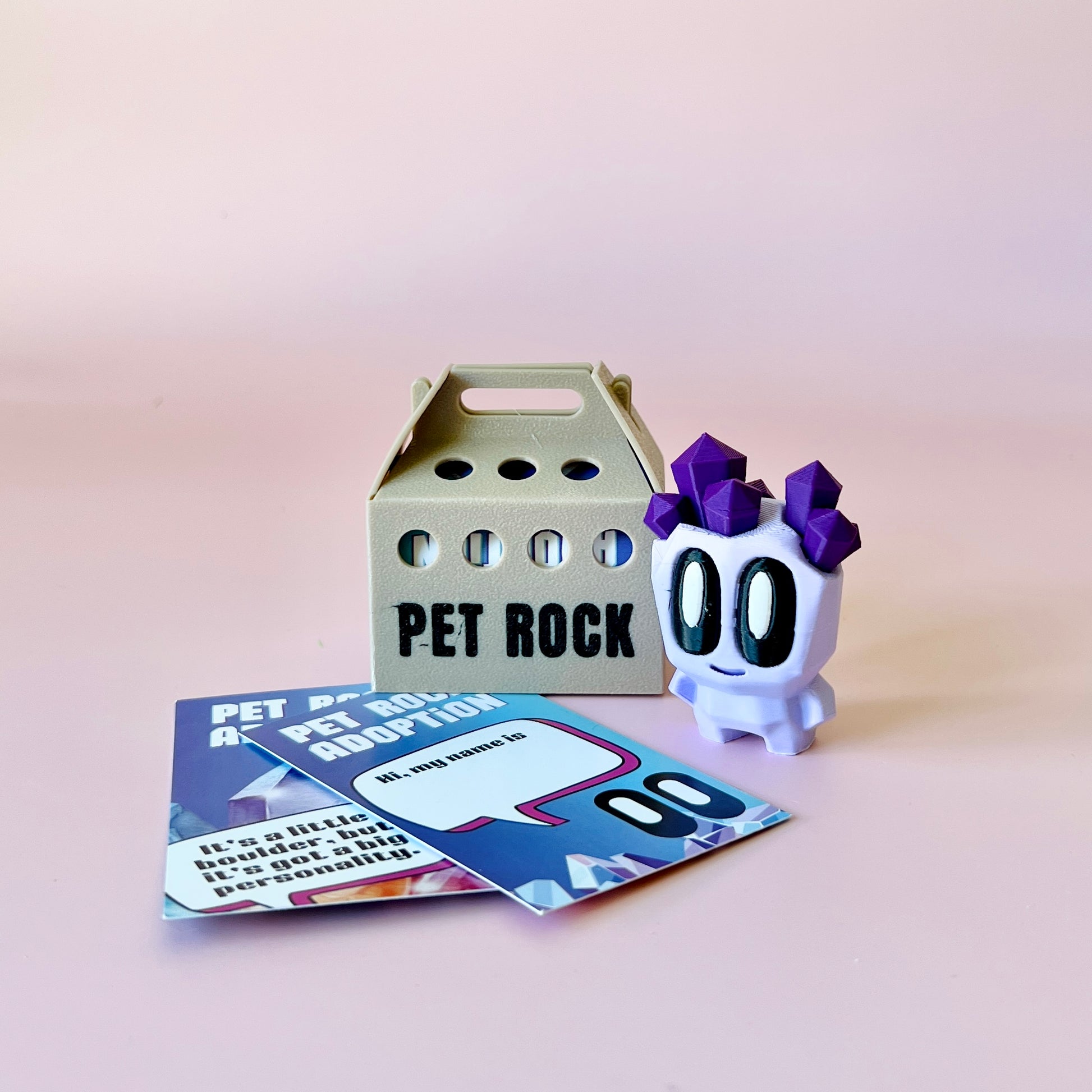 A whimsical character with purple crystals on its head beside a cardboard carrier and colorful adoption cards.