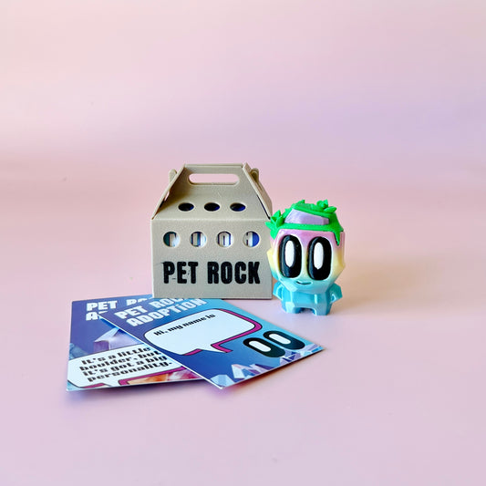 Colorful, cartoonish creature with large eyes and green accents, alongside an adoption box and playful cards on a pink backgr