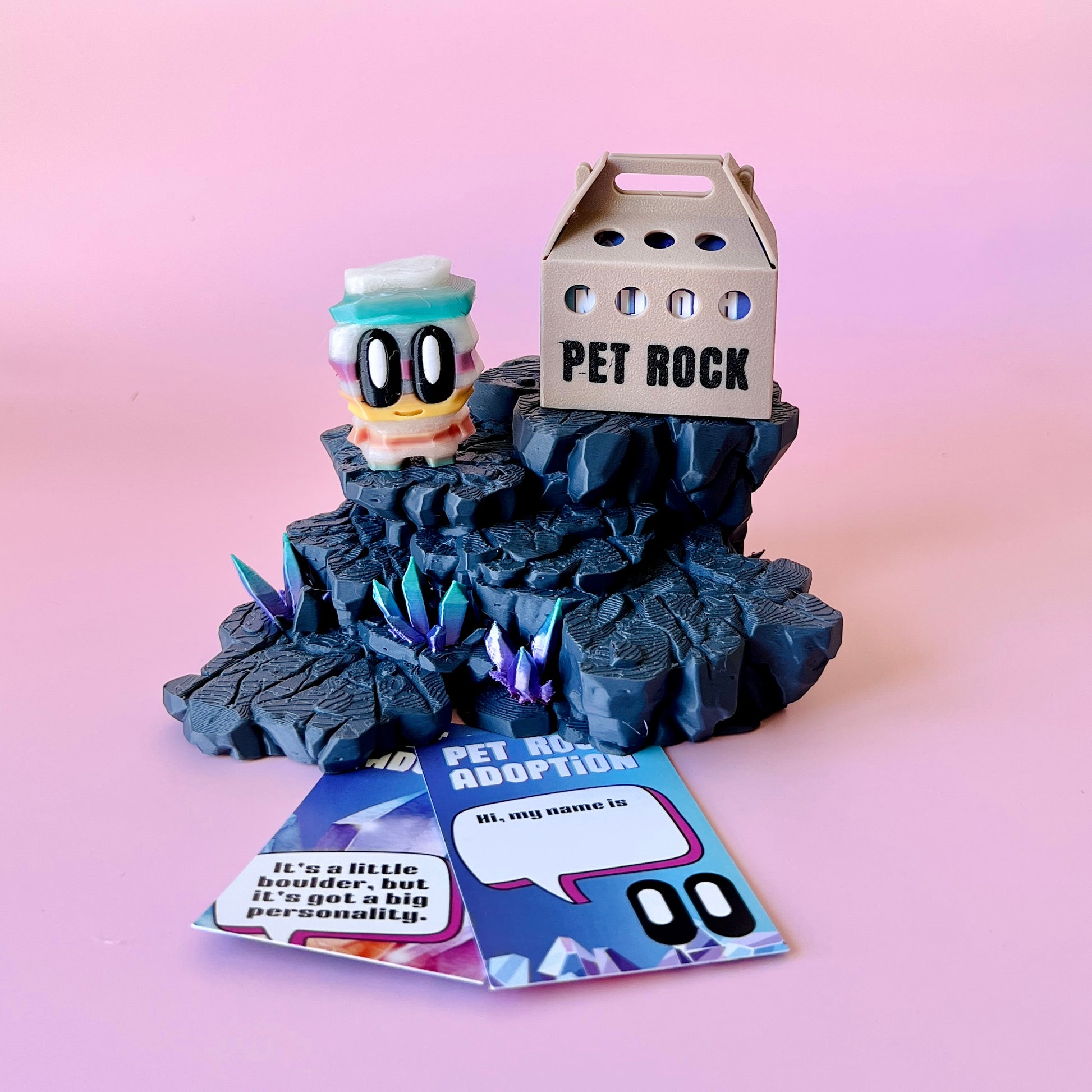 Colorful character atop rocky terrain with sparkling crystals and a whimsical adoption box, set against a pink background.