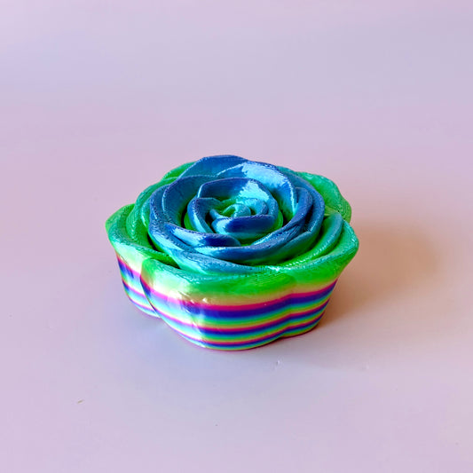 A vibrant, multi-colored rose with blue and green hues, featuring swirling patterns and glossy petals.