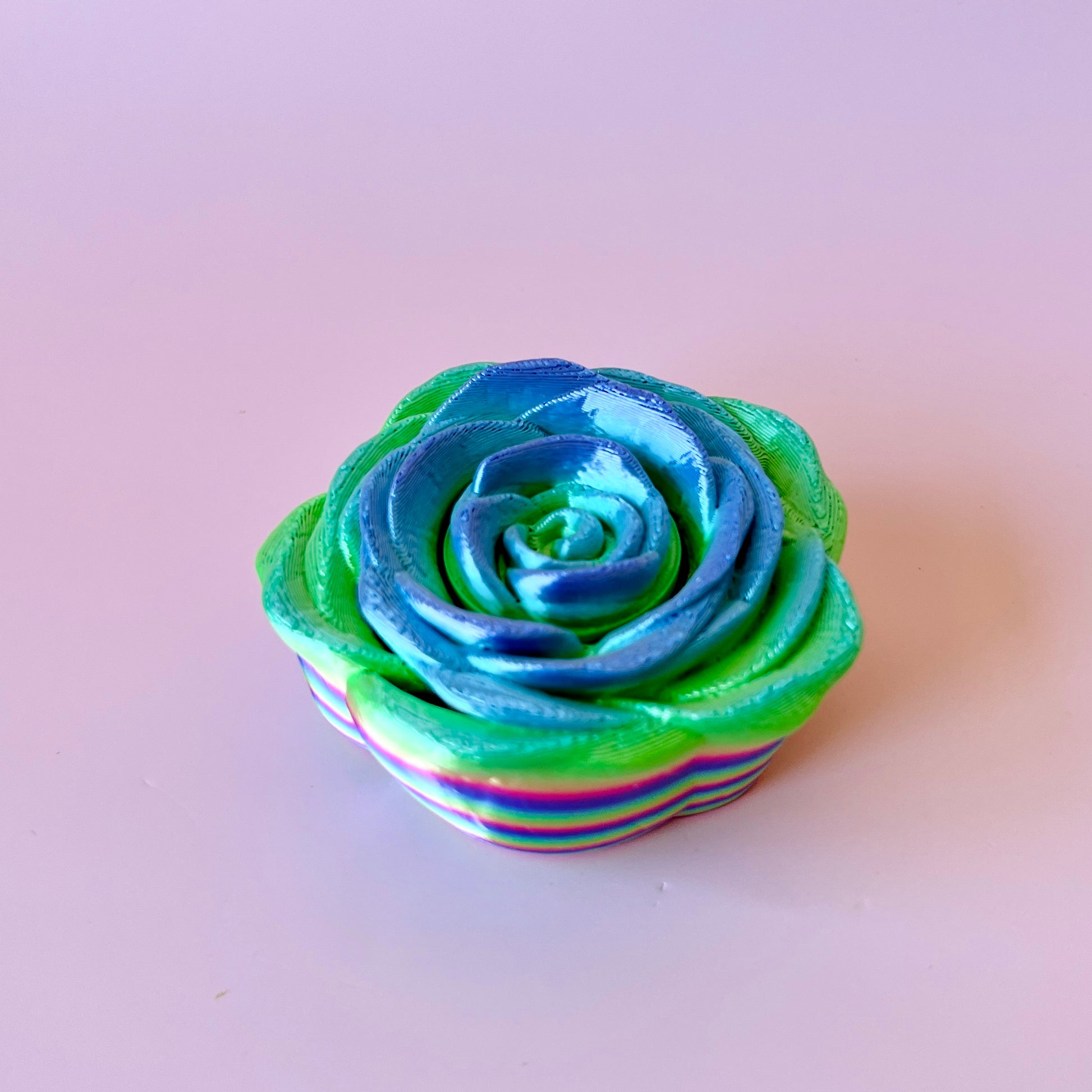 A vibrant, multi-colored rose with blue and green hues, resting on a light background.