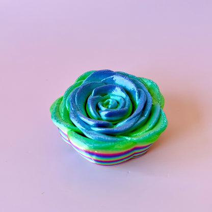 A vibrant, multi-colored rose with blue and green hues, resting on a light background.