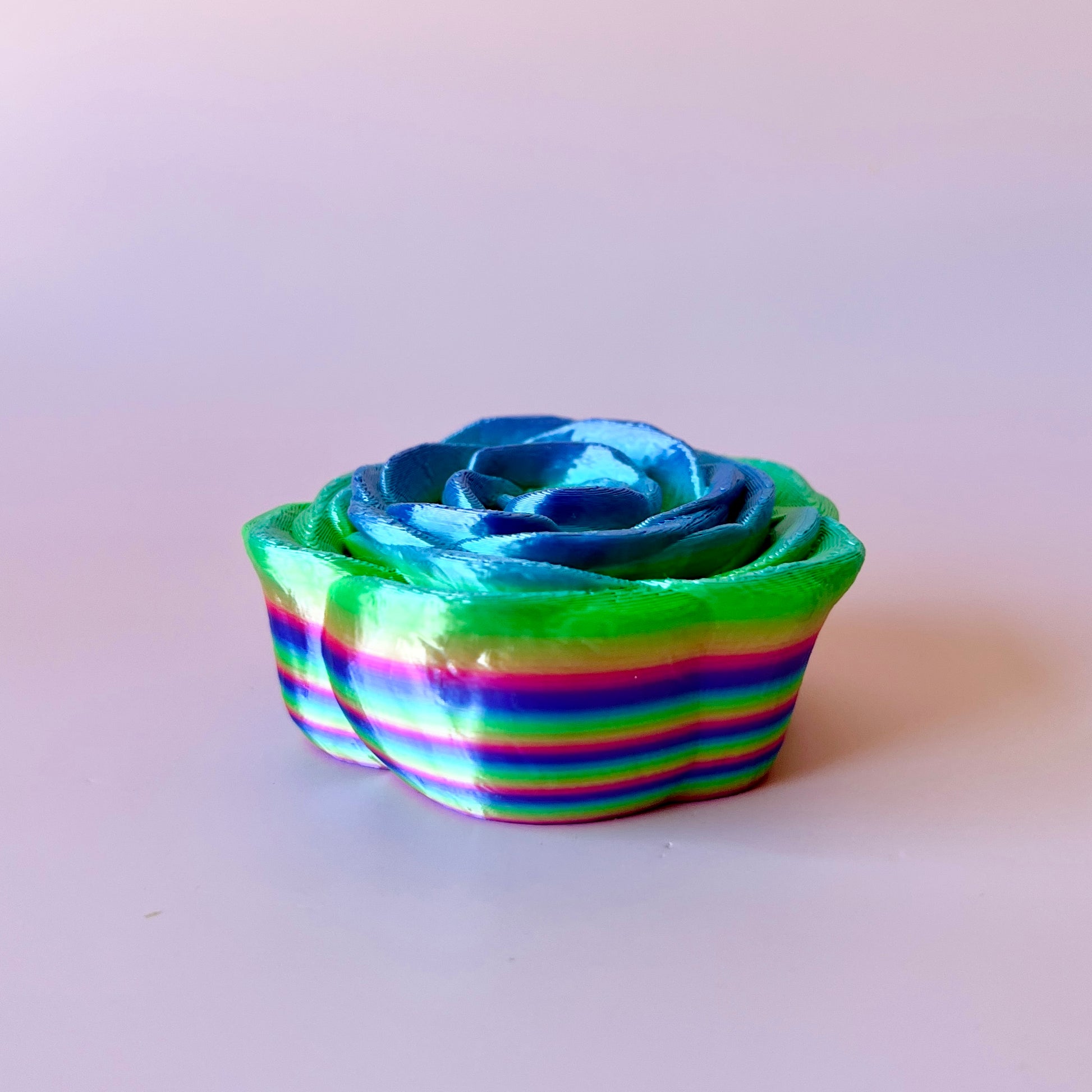 Colorful layered rose with blue and green hues, displaying intricate petal details against a soft background.