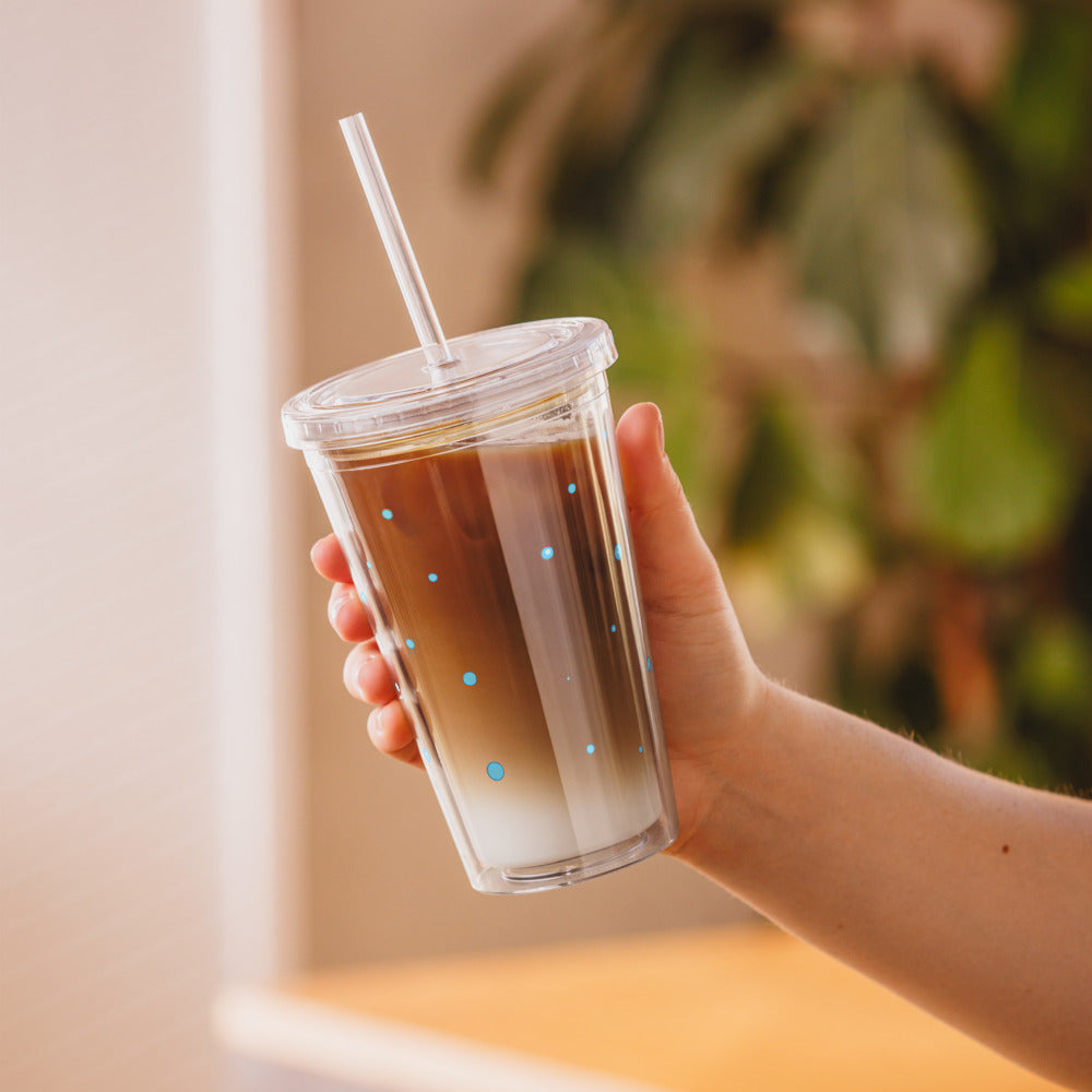 Clear tumbler with blue dots, held in a hand, filled with a layered beverage, showcasing a playful and vibrant style.