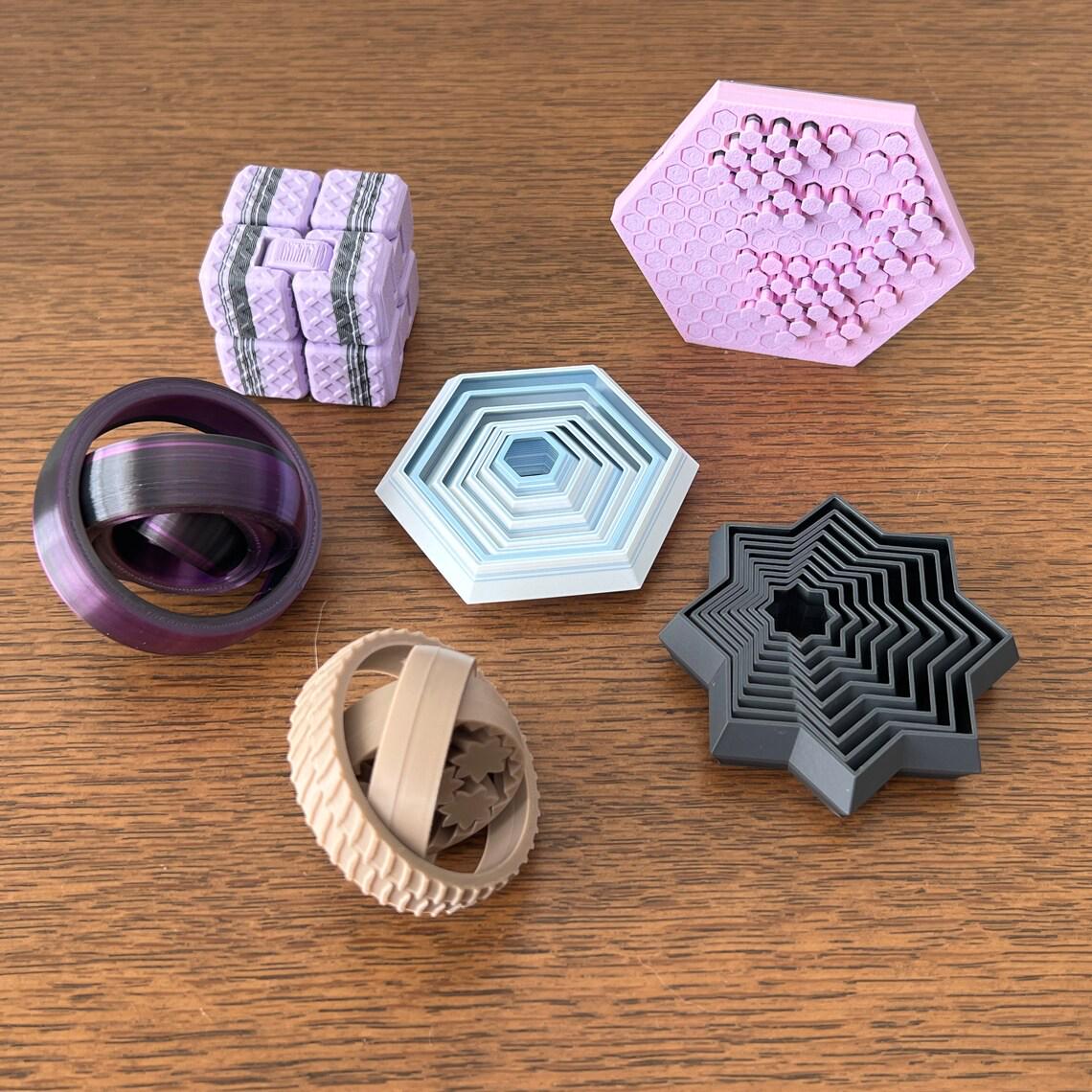 Colorful 3D-printed fidgets in various shapes: star, hexagon, infinity cube, and more, offering tactile engagement.