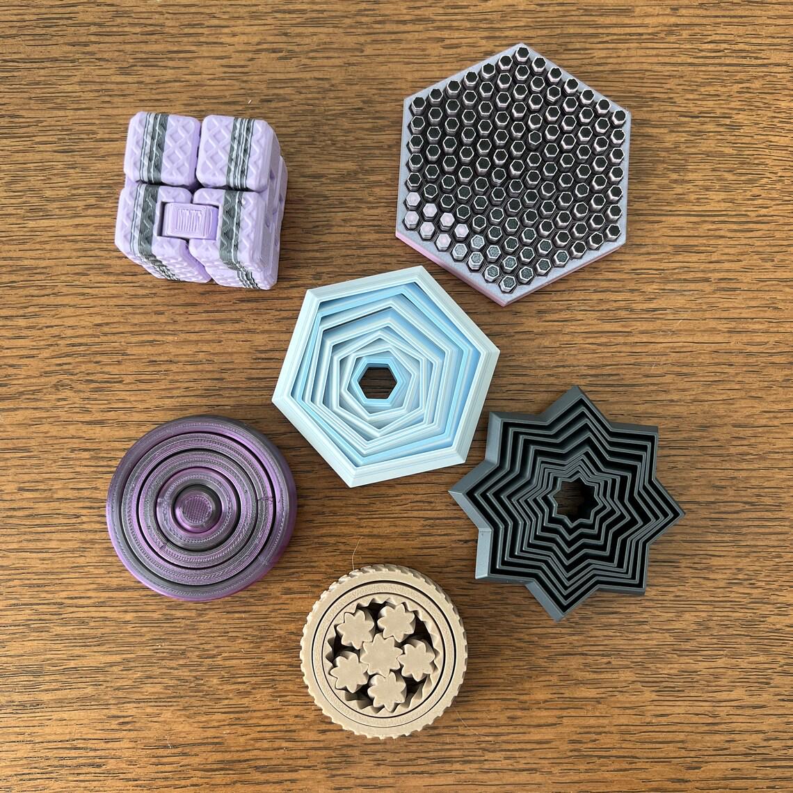 Colorful 3D-printed fidget shapes: a cube, hexagons, a star, and a round design, all on a wooden surface.