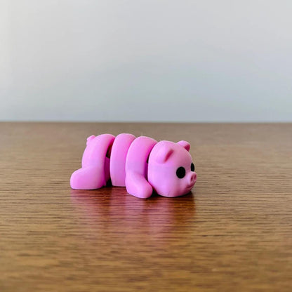 Articulated pink pig figure with black eyes, resting on a wooden surface, perfect for sensory play or collection.