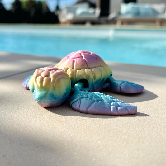 Colorful 3D-printed sea turtle resting on a surface, with intricate details and a serene pool backdrop.