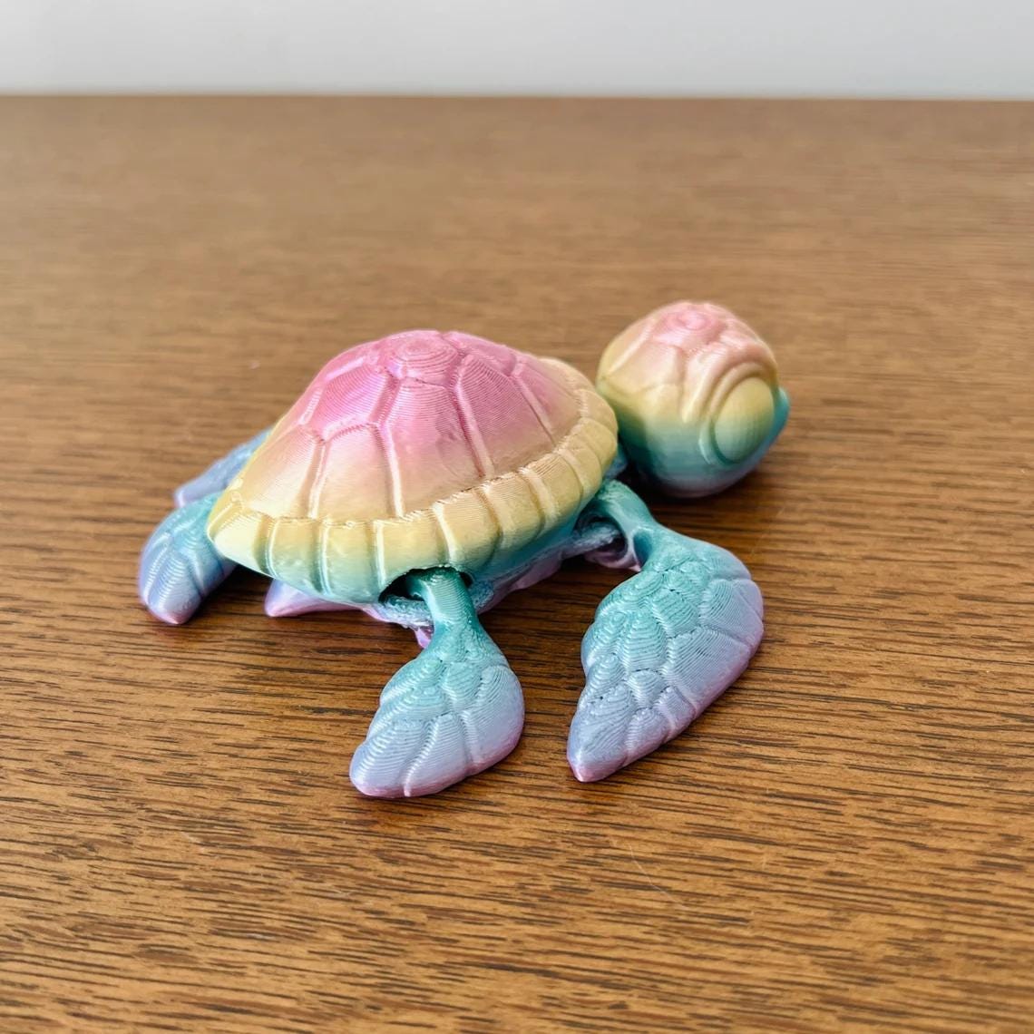 Colorful 3D-printed sea turtle figurine with a pink and teal finish, resting on a wooden surface.