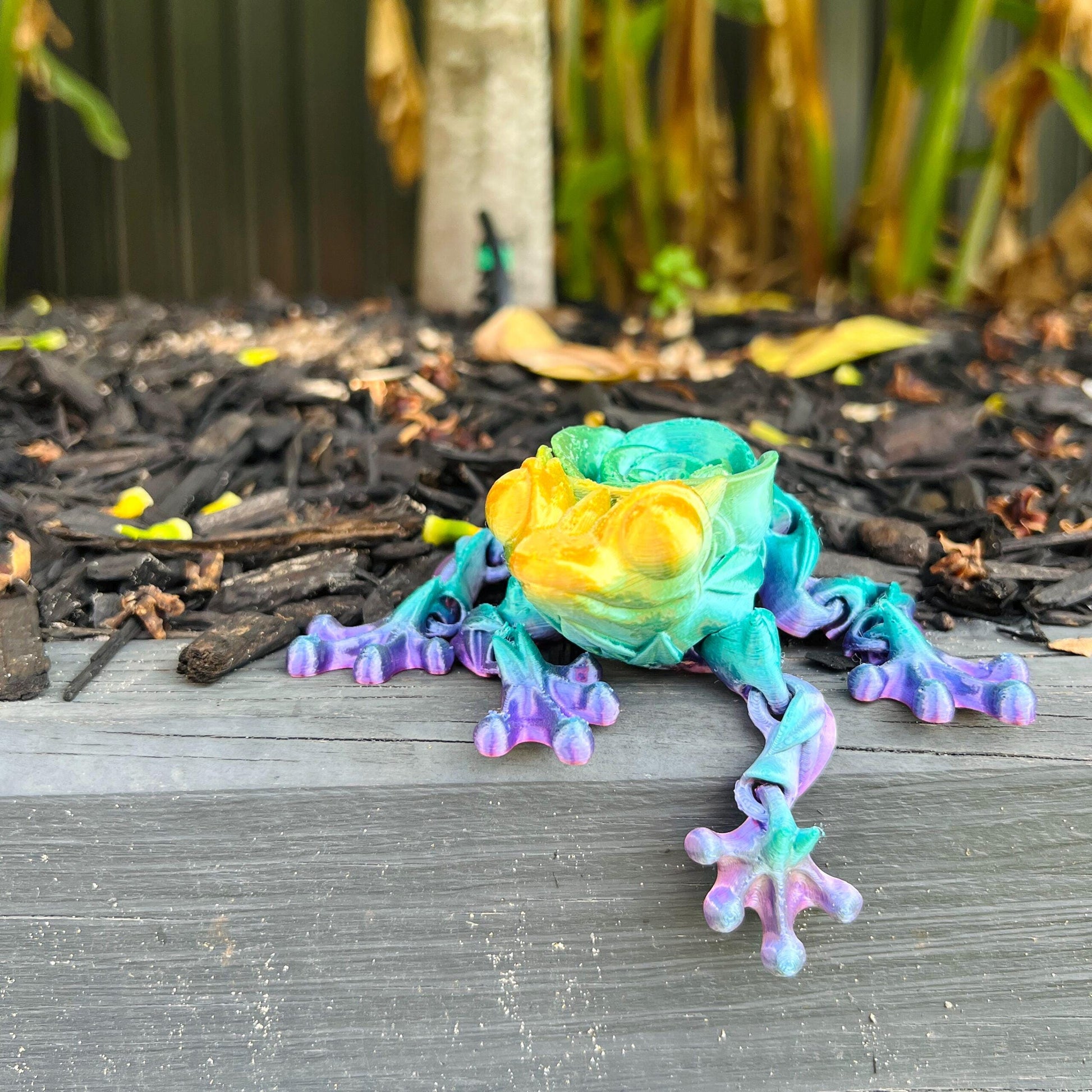 Colorful articulated frog figurine with vibrant hues of green, yellow, and purple, resting on a wooden surface.