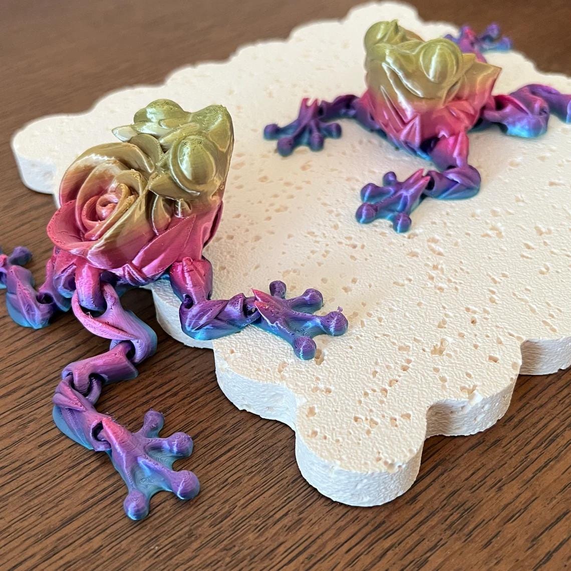 Articulated rose frog figurines in vibrant colors, showcasing intricate details, resting on a textured, light surface.