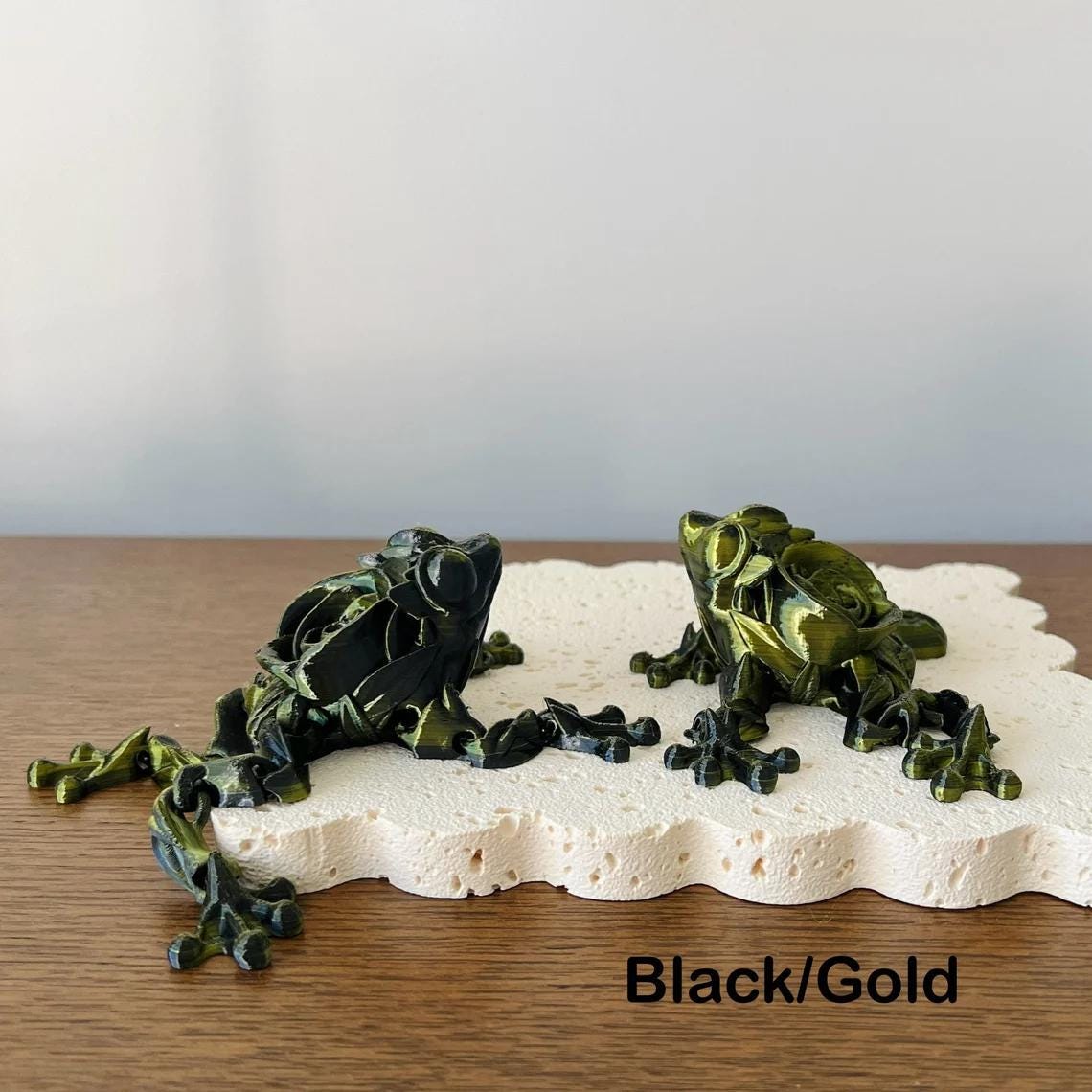 Articulated figurine of a rose frog in black and gold, showcasing intricate detailing on a textured surface.