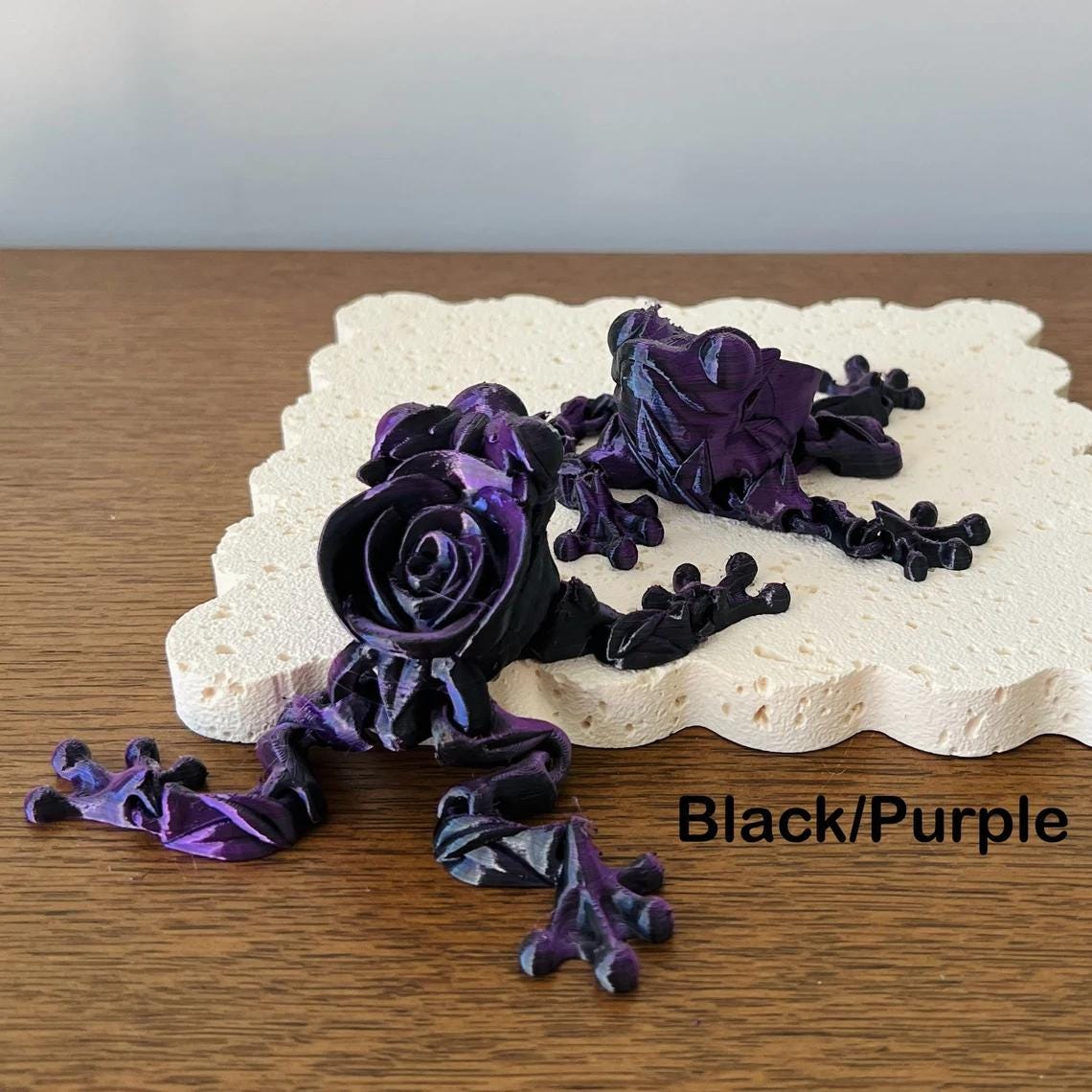 Articulated rose frog figurine in black and purple, showcasing intricate floral details on a textured surface.