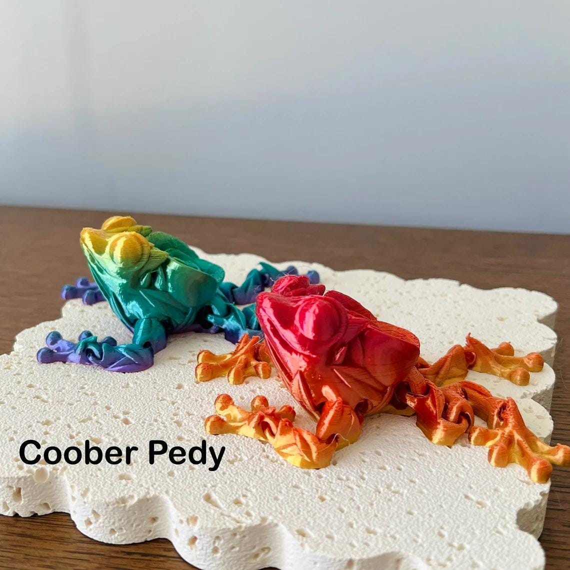 Colorful articulated rose frogs in turquoise and red resting on a textured white surface, showcasing vibrant details.