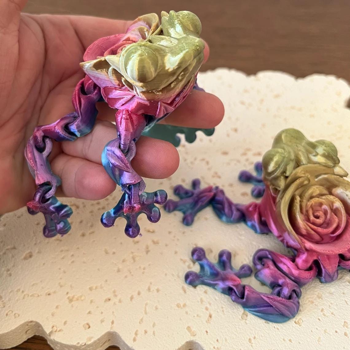 Articulated Rose Frog figurine in vibrant colors, showcasing intricate details and customizable features, held in a hand.