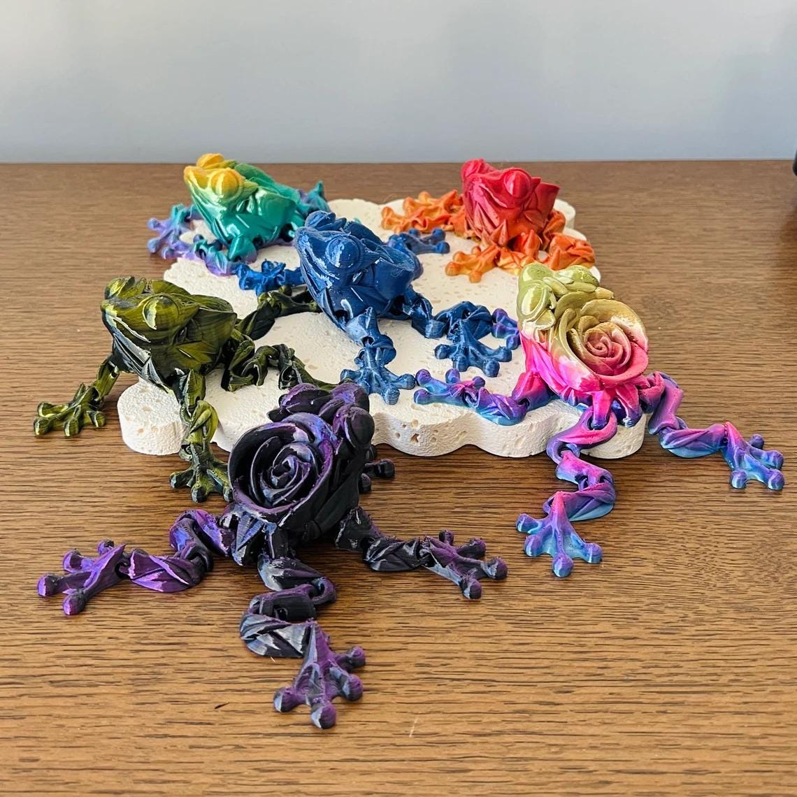 Colorful articulated frogs with rose details, showcasing vibrant hues on a textured surface. Perfect for collectors!