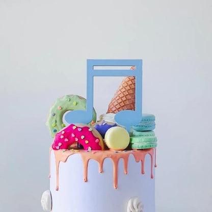 Colorful music note topper on a cake with playful sweets like cookies and macarons, adding fun to any celebration.