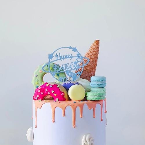 Whimsical cake topper featuring a planet, stars, spaceship, and "happy birthday" text atop a colorful confectionery display.