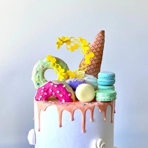Bright honeycomb topper with cute bees atop a colorful, drippy cake featuring macaroons and donuts for festive celebrations.