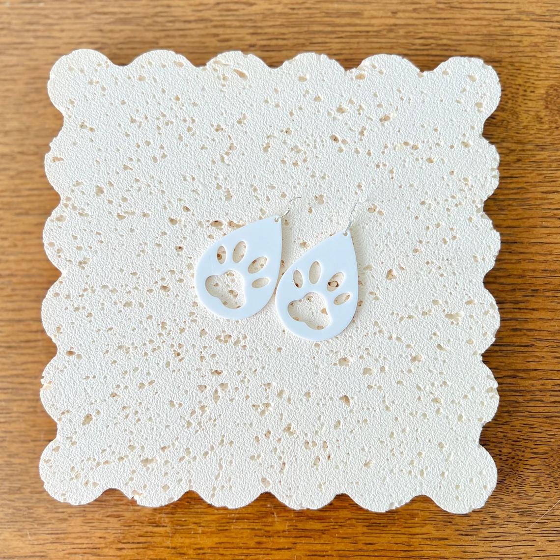 White paw print dangle earrings on a textured background, featuring sterling silver hooks for a stylish touch.