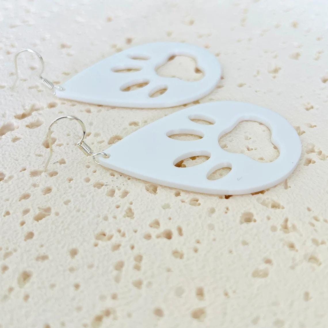 White paw print dangle earrings with sterling silver hooks, showcasing a playful and elegant design on a textured surface.