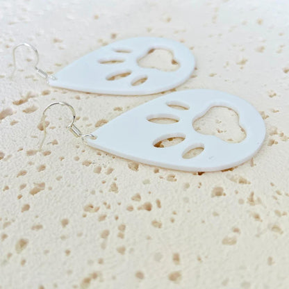 White paw print dangle earrings with sterling silver hooks, showcasing a playful and elegant design on a textured surface.