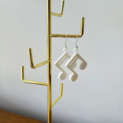 White music note dangle earrings hanging from a gold display stand, showcasing their elegant and lightweight design.