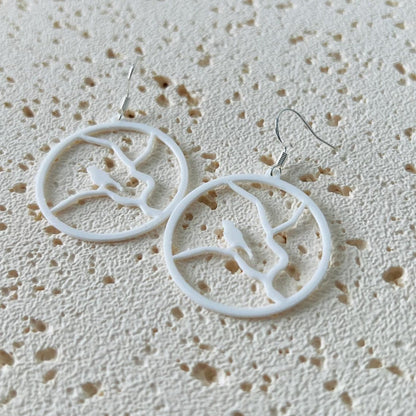 White dangle earrings featuring a bird perched on a branch, crafted from lightweight materials with sterling silver hooks.
