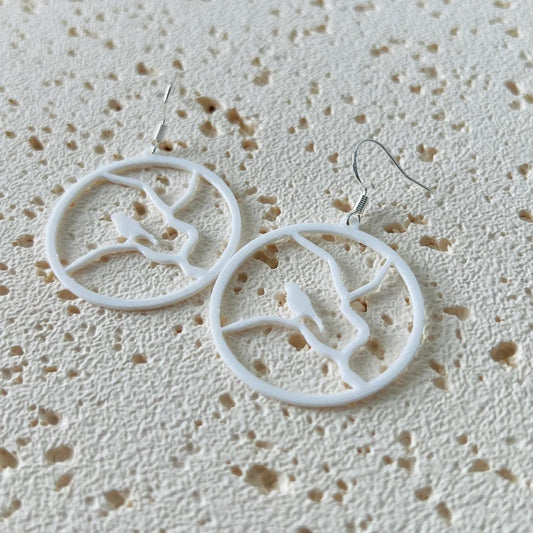 White dangle earrings featuring a bird perched on a branch, crafted from lightweight materials with sterling silver hooks.