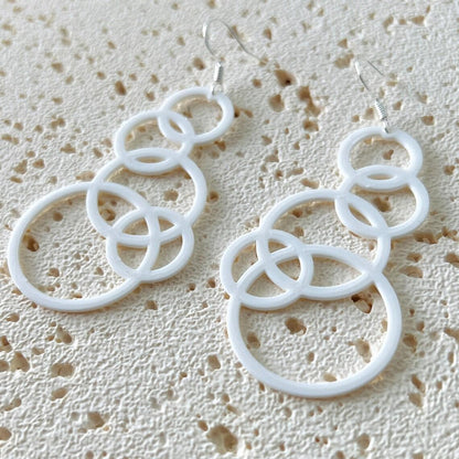 White bubble dangle earrings with multiple interlocking circles, hanging from sterling silver hooks, on a textured background