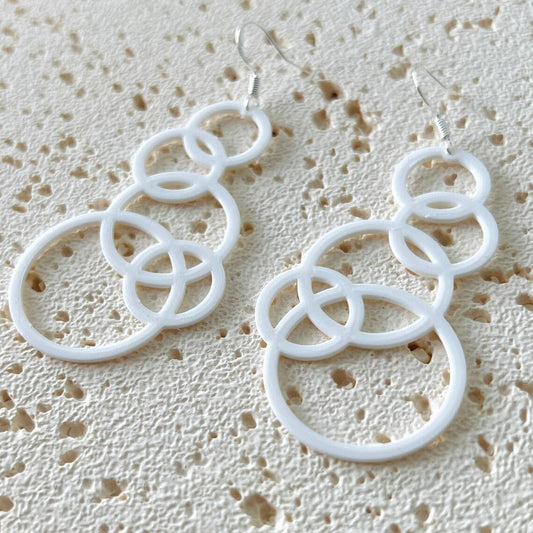 White bubble dangle earrings with multiple interlocking circles, hanging from sterling silver hooks, on a textured background
