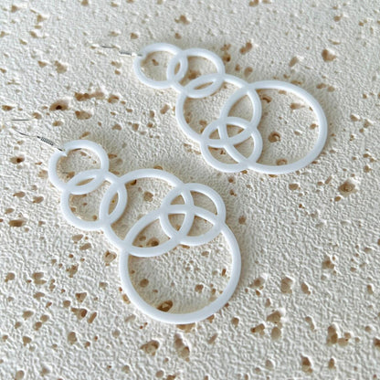 White bubble dangle earrings with multiple interlinked circles, hanging from sterling silver hooks on a textured surface.