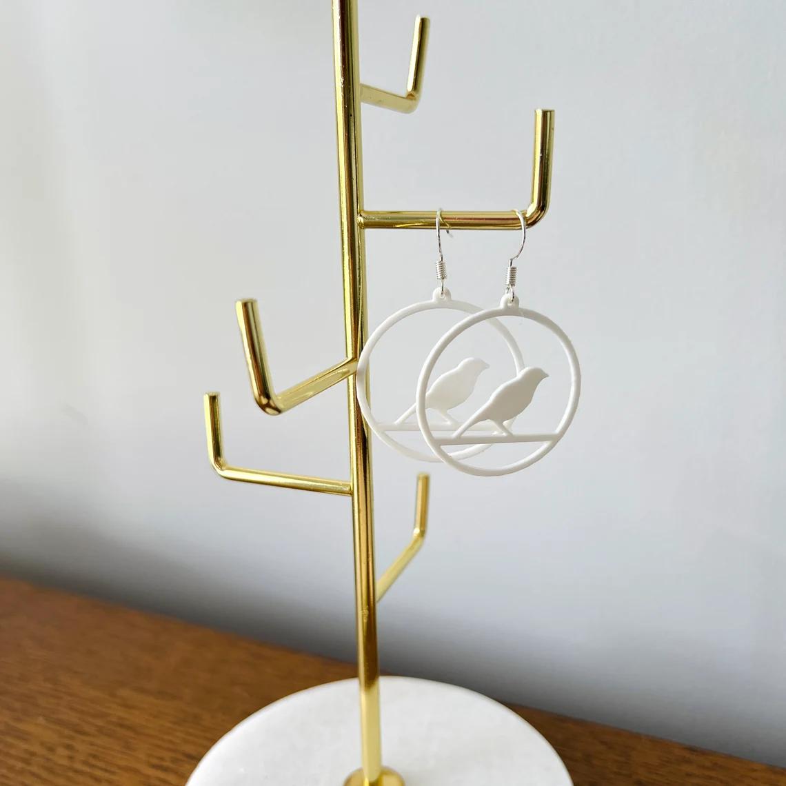 Elegant white bird dangle earrings hung on a sleek gold display stand, embodying charm and sophistication.
