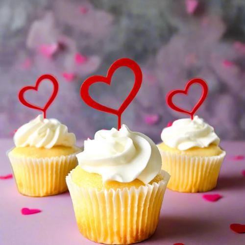 Three cupcakes topped with playful red heart picks, surrounded by pink heart confetti, perfect for celebrations.