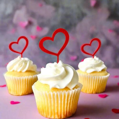 Three cupcakes topped with playful red heart picks, surrounded by pink heart confetti, perfect for celebrations.