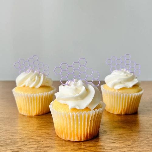 Whimsical honeycomb toppers in lavender atop vanilla cupcakes with swirls of creamy frosting, perfect for celebrations.