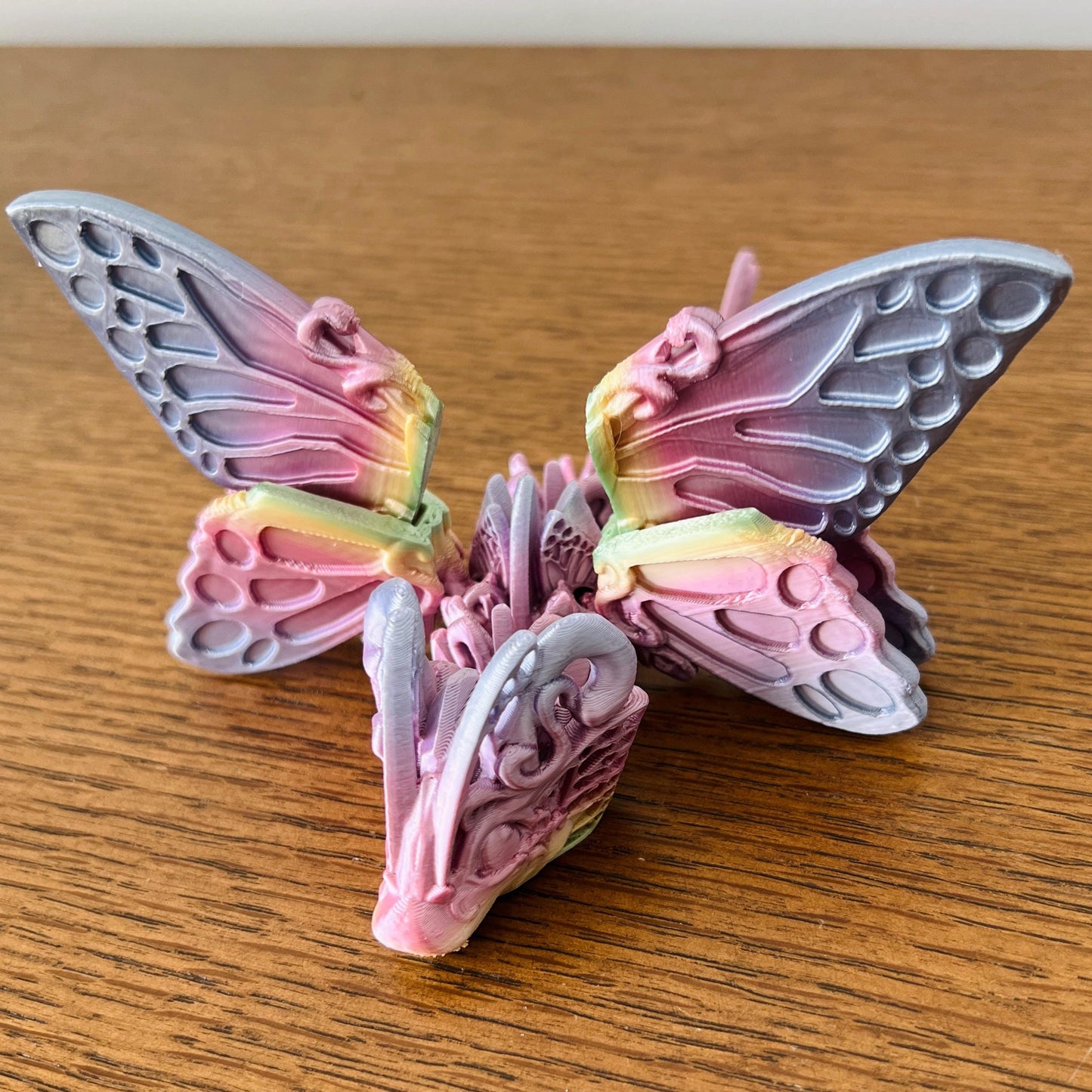 Colorful dragon with butterfly wings, featuring intricate patterns and a whimsical design, resting on a wooden surface.