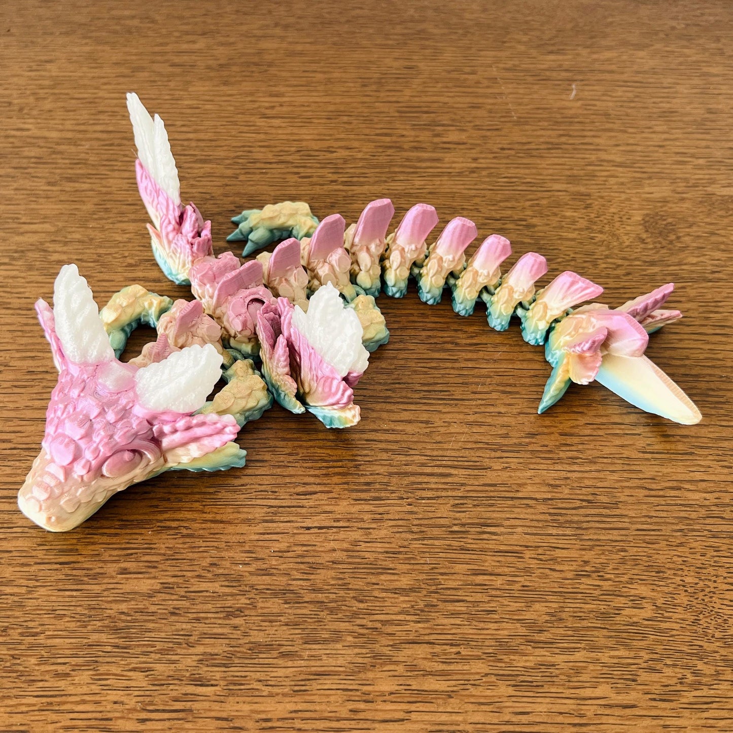 Whimsical dragon with axolotl features, elegant wings, and intricate pastel details resting on a wooden surface.