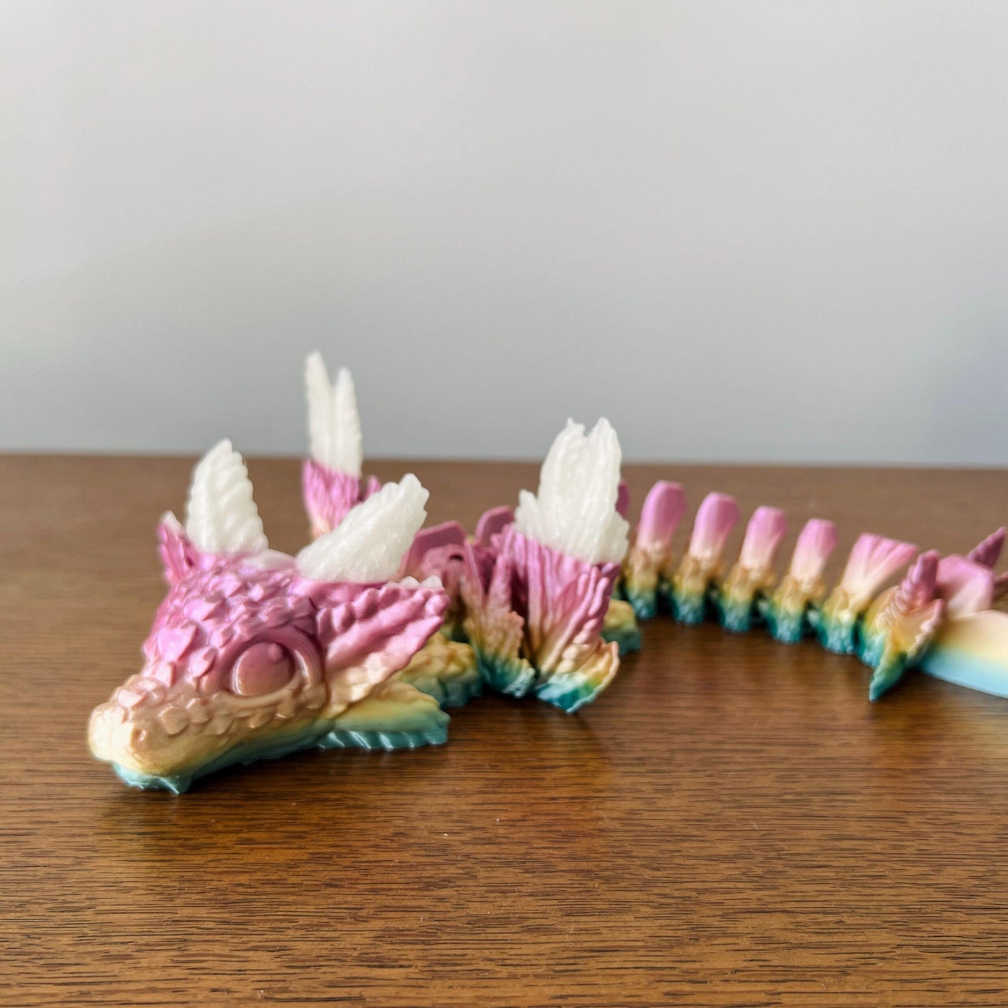 Whimsical pink and white dragon with elegant wings, featuring intricate scales and a playful, enchanting design.