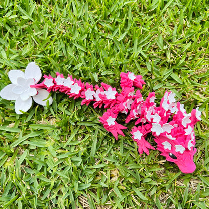 A vibrant pink dragon adorned with white cherry blossoms, resting on a lush green grass backdrop.