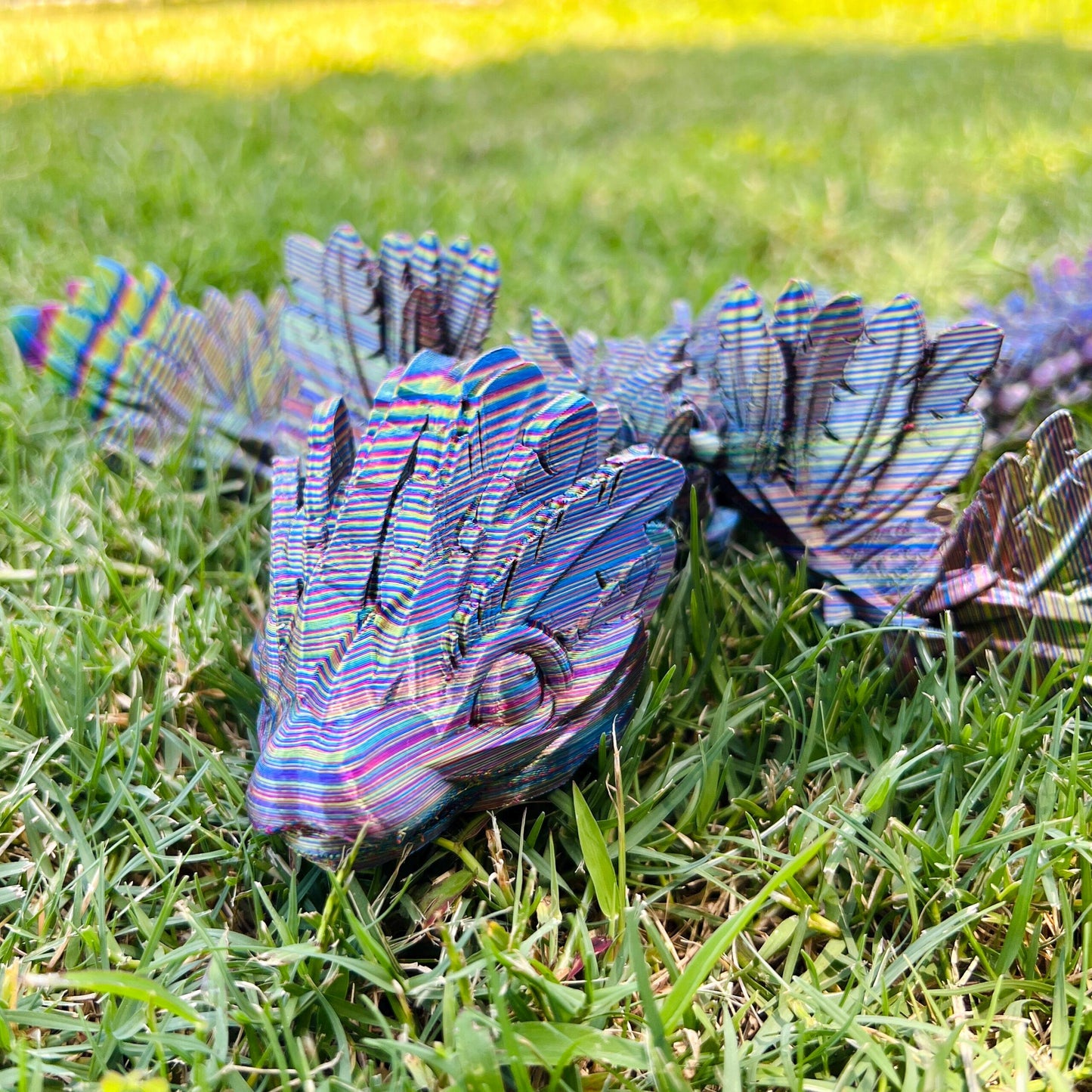 A vibrant, sleek dragon with intricate, colorful wings rests on lush green grass, embodying elegance and mystery.