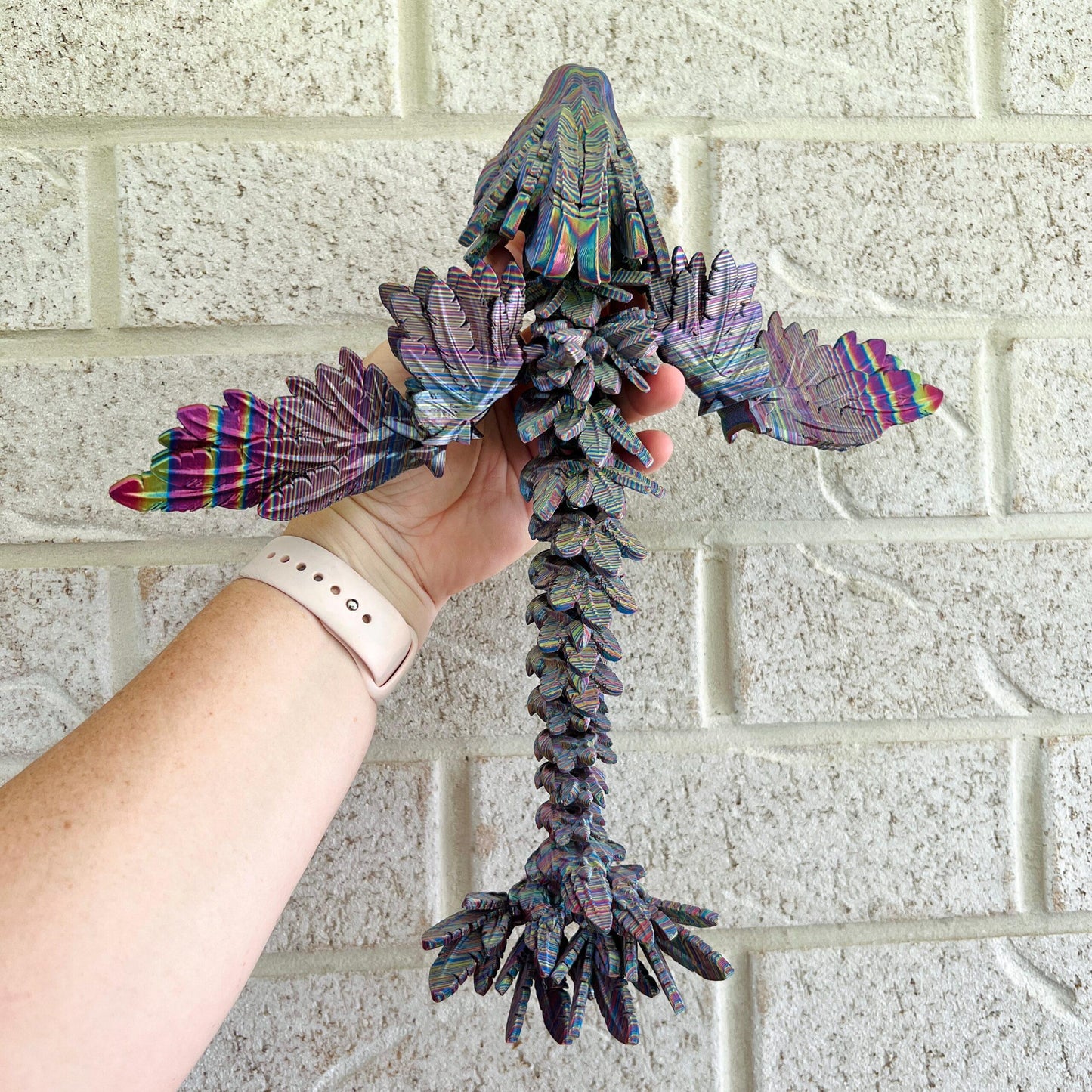 Sleek, colorful dragon with intricate scales and elegant wings, held against a textured wall.