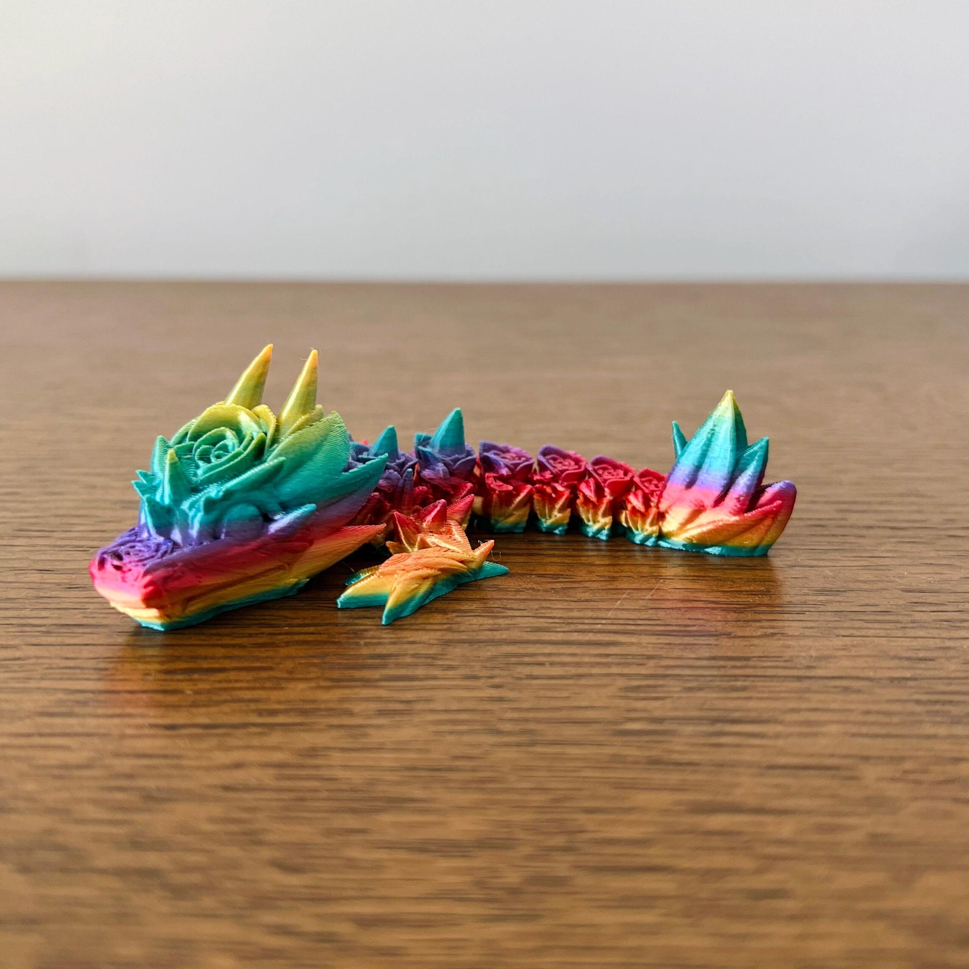 Colorful, intricately detailed dragon with rose accents, showcasing elegance and fantasy on a wooden surface.