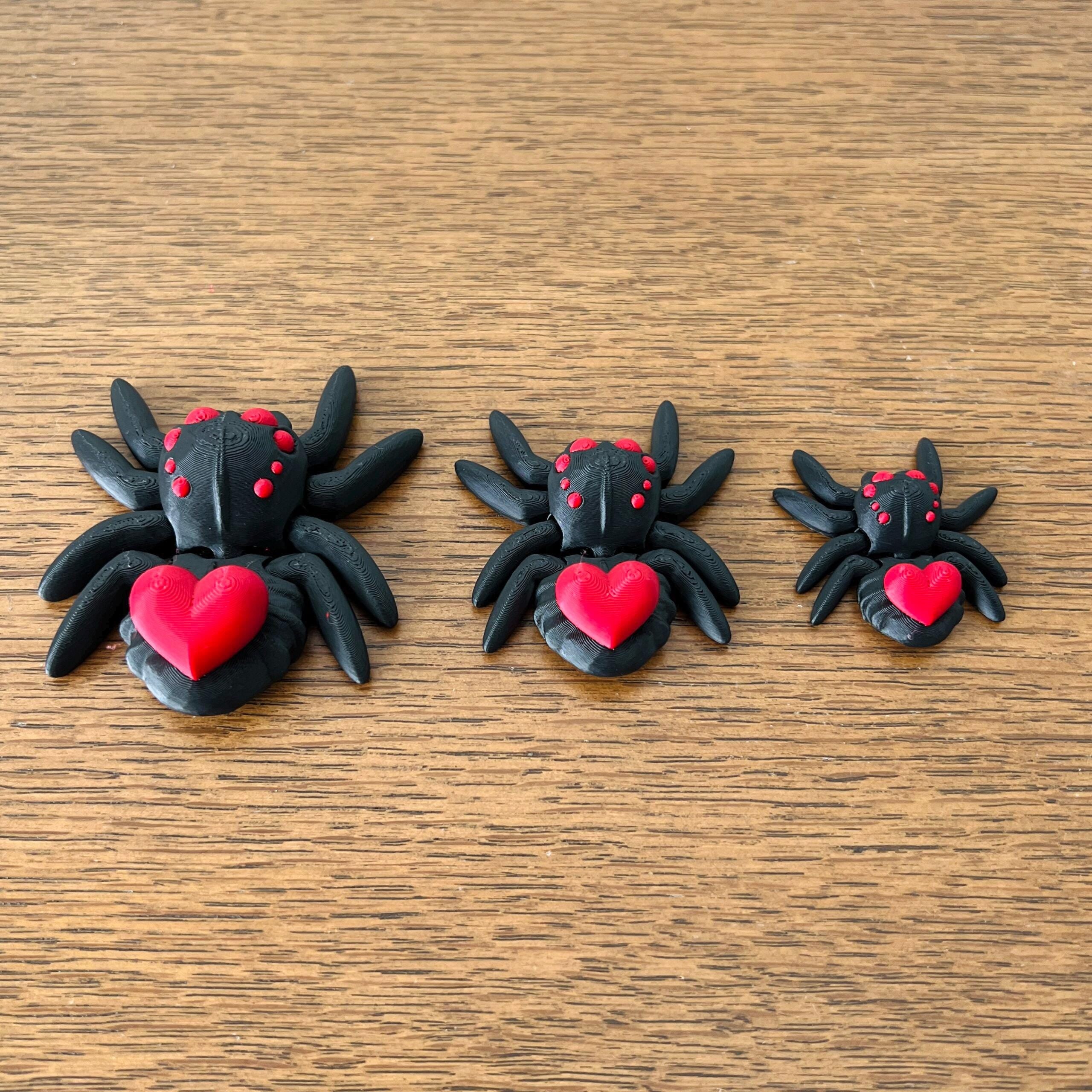 Three adorable black spiders with red hearts on their backs, varying in size, resting on a wooden surface.