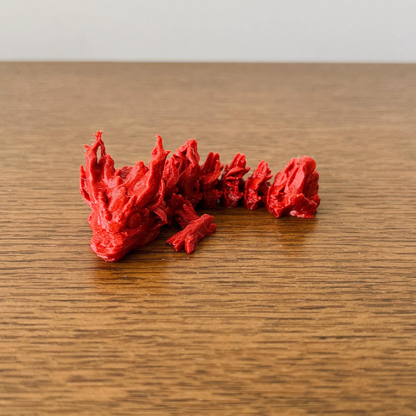 A charming red dragon with detailed scales and spiky features, resting on a wooden surface, evoking a woodland fantasy.