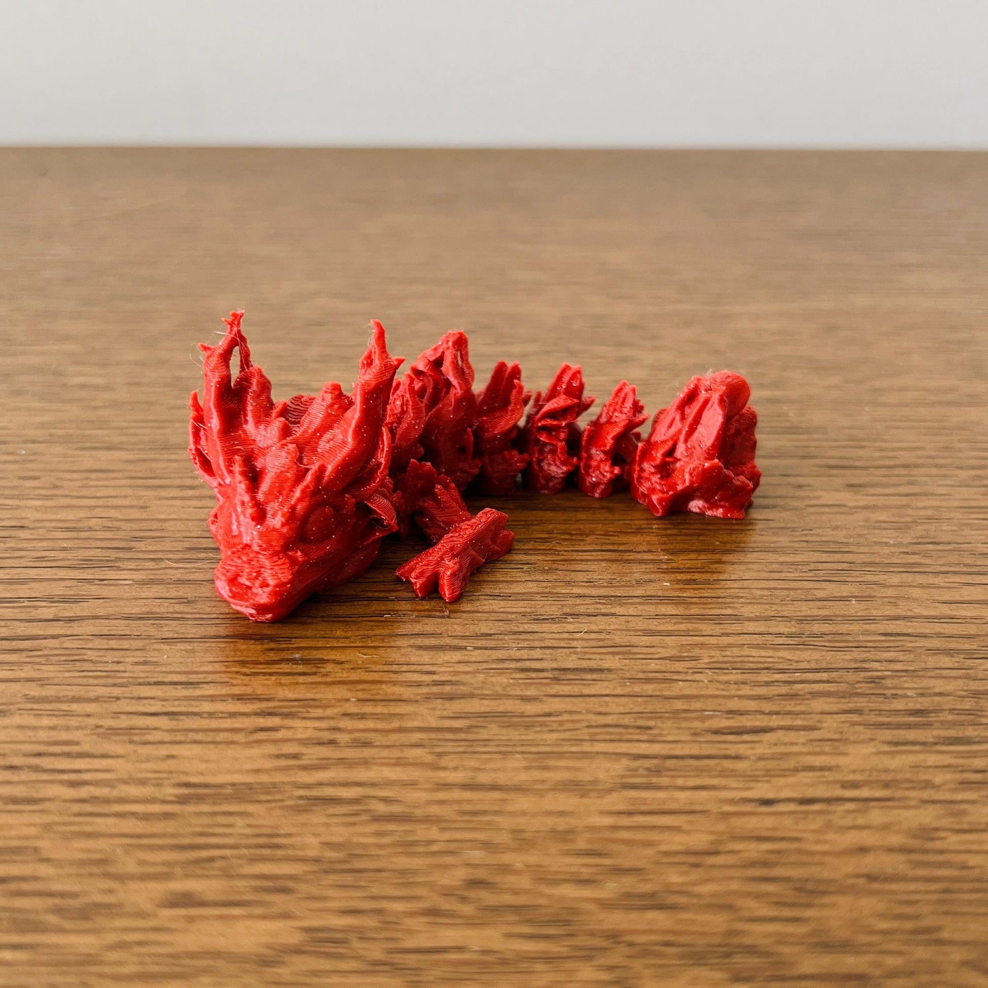 A charming red dragon with detailed scales and spiky features, resting on a wooden surface, evoking a woodland fantasy.